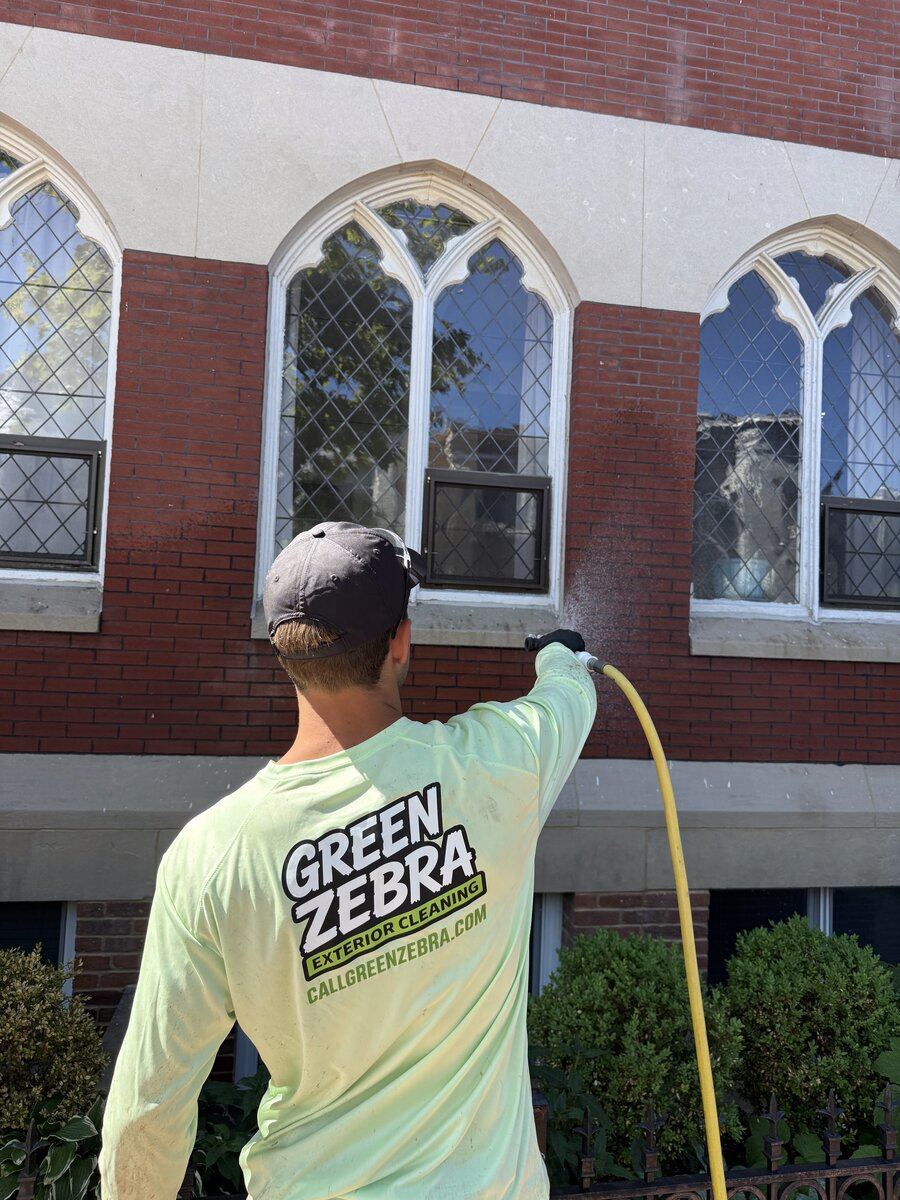 Green Zebra crew member cleaning a brick building