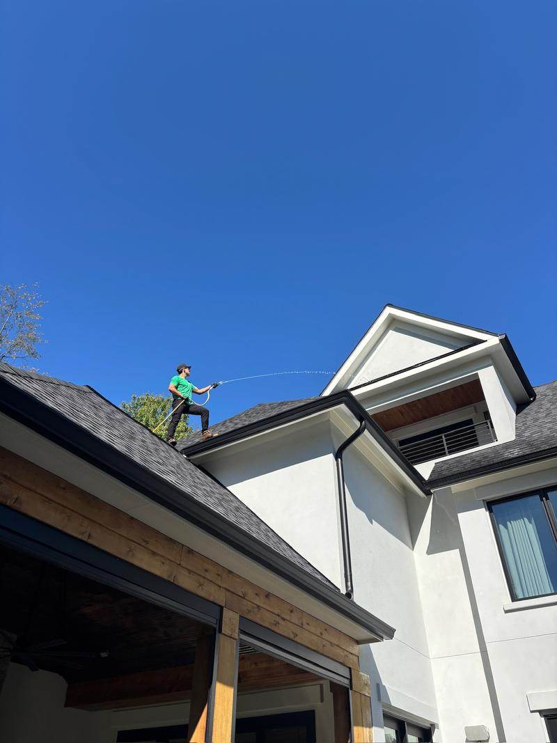 Green Zebra technician on a roof soft washing a white stucco home