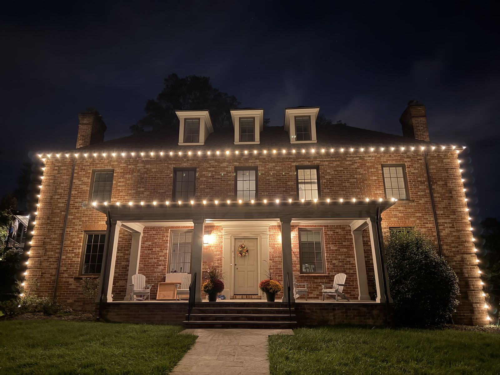 Brick colonial in Arlington, Virginia at night with warm white C9 lights along the roofline, porch roof, and corners, installed by Green Zebra