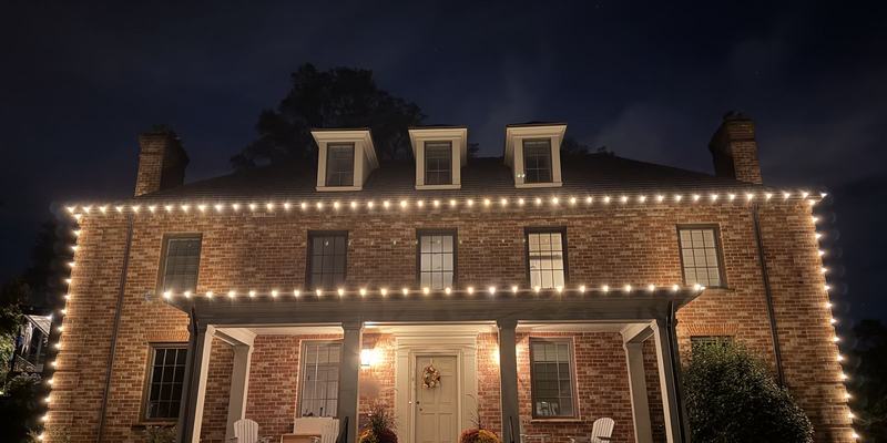 Brick colonial at night with warm white lights along the roofline and porch, installed by Green Zebra